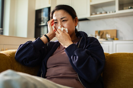 Sick woman with tissue resting on sofa at home
