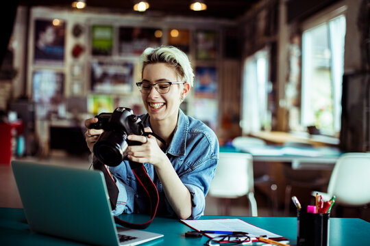 Smiling photographer reviewing camera at laptop in creative studio