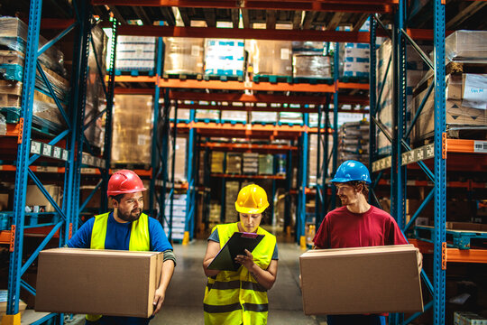Workers carrying boxes with supervisor checking inventory in warehouse