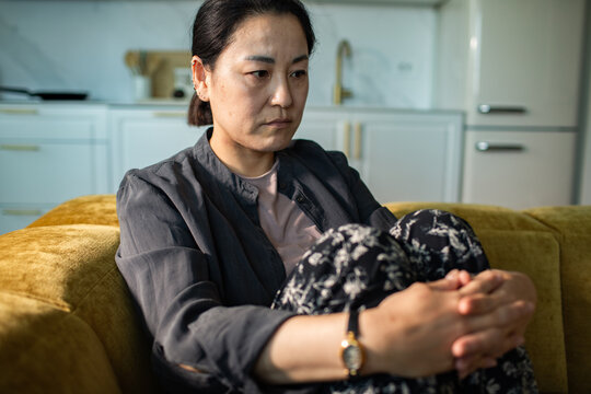 Sad woman hugging knees on couch at home