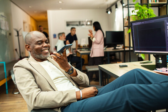 Smiling businessman using smartphone speaker in modern office