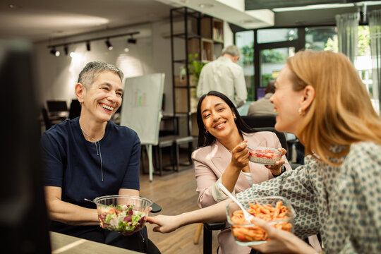 Smiling coworkers sharing healthy lunch in modern office