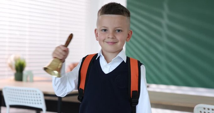 Cute boy ringing school bell in classroom