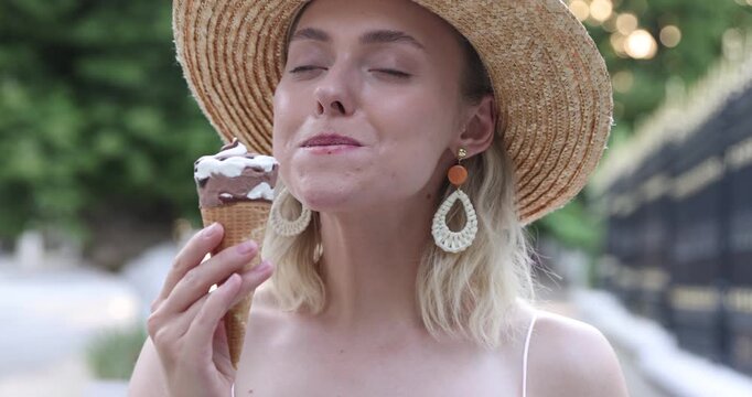 Happy woman in hat eating delicious ice cream outdoors, camera moving forward and backwards