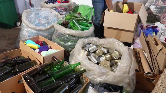 Waste recycling center, worker sorting recyclable materials including plastic, tin cans, cardboard boxes, textiles, shoes, glass bottles and old electronics