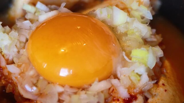 焼肉店で味わう旨辛スンドゥブチゲに乗った生卵のクローズアップ
