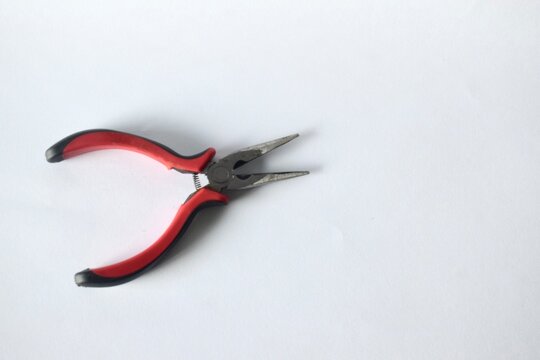 High angle view of single spring-loaded long needle nose pliers with black and red insulated rubber handles on a plain white surface.