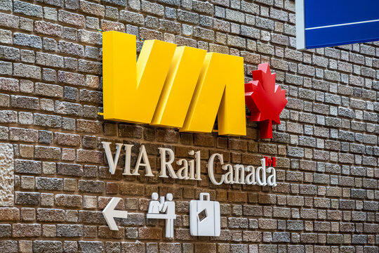 Quebec City, QC, Canada. July 30, 2026. Angled close-up view of the VIA Rail Canada logo and passenger directional sign on a brick wall.