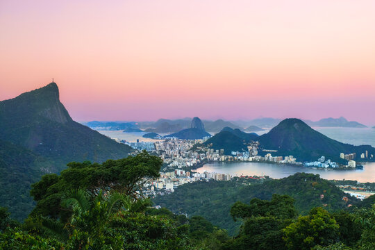 Panoramic view of Rio de Janeiro at twilight from Vista Chinesa, featuring Corcovado Mountain with Christ the Redeemer, Rodrigo de Freitas Lagoon, and Sugarloaf Mountain under a pastel sky, Brazil.