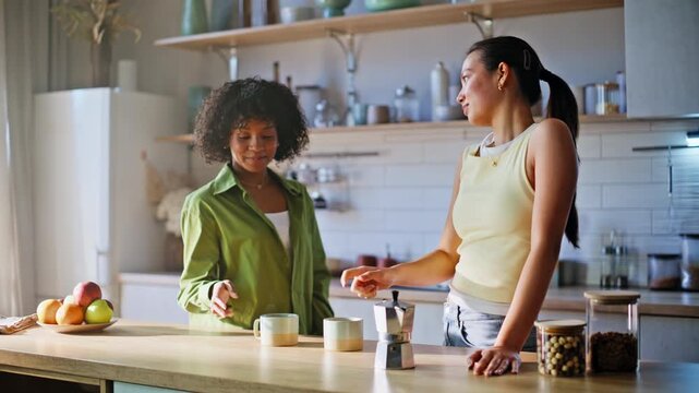 Multiethnic friends chatting over coffee. Two women drinking brew home kitchen.