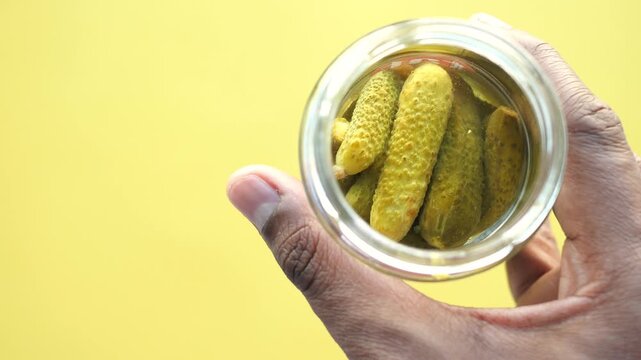 Close up of person holding jar of pickled cucumbers against yellow background