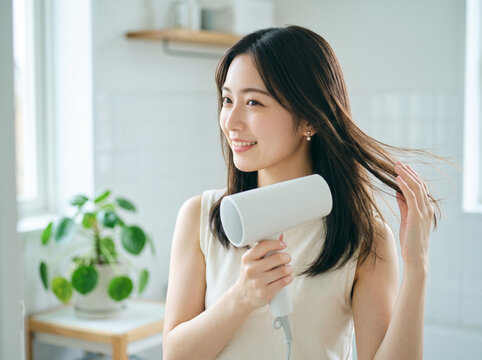 白い服を着て髪の毛を風になびかせながらドライヤーをかける女性