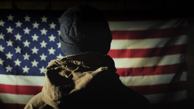 Person standing in dark room looking at illuminated united states flag.