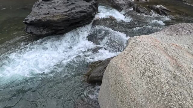 Fast flowing mountain stream rushing over large granite boulders in natural daylight, 4K b-roll