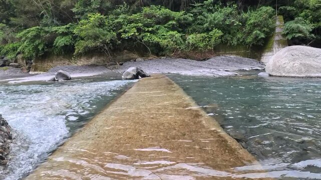 Shallow river water flowing over a submerged concrete crossing in a lush forest, 4K b-roll
