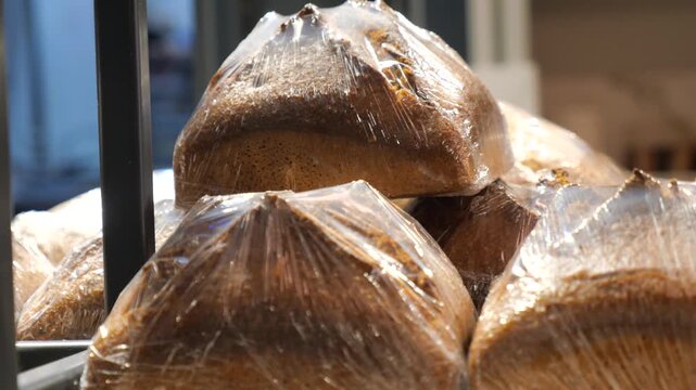 Freshly baked rye bread loaves wrapped in plastic film on bakery shelf, ready for sale at grocery store