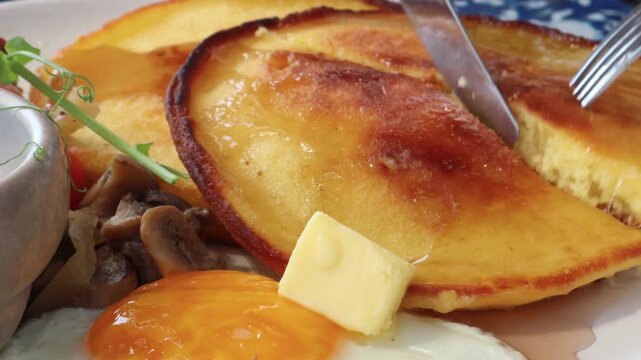 Someone is having breakfast, enjoying honey pancakes, a sunny-side-up egg, a fried sausage, and barbecue sauce