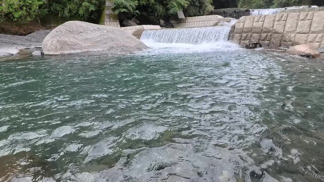 Clear turquoise mountain stream flowing gently below a small stone waterfall in daylight, 4K b-roll