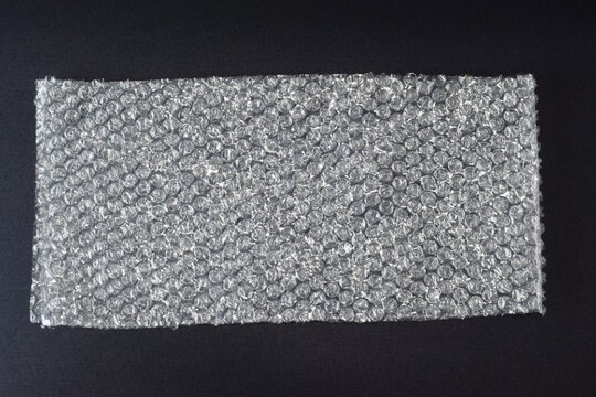 A flat overhead view of a square sheet of protective bubble wrap packaging material centered on a plain black background.