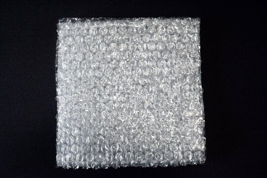 A flat overhead view of a square sheet of protective bubble wrap packaging material centered on a plain black background.