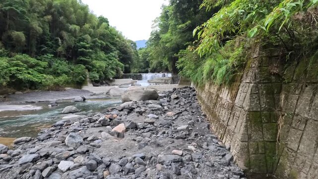 Flowing mountain stream through rocky riverbed surrounded by lush green forest, 4K b-roll