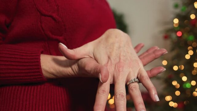 Close-up of a woman showing off her engagement ring in front of a Christmas tree with blurred lights in the background.
