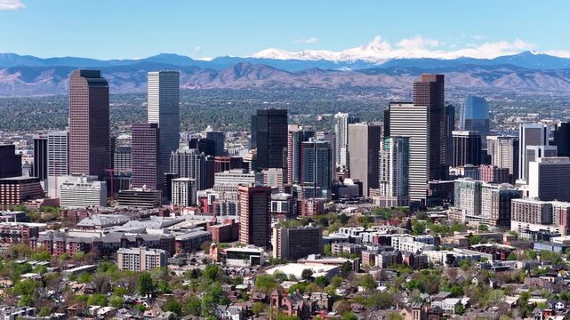 Aerial drone footage of the Denver skyline with the snow capped Rocky Mountains visible in the background under clear skies