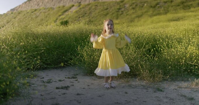 Little girl in yellow dress walking through blooming meadow in warm evening light