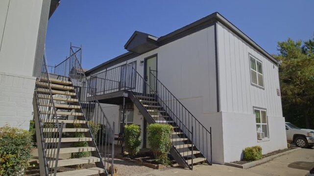 Sunny daytime shot of a duplex-style multifamily housing building with metal exterior stairs and surrounding greenery.