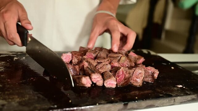 Cutting Seared Beef Strips into Cubes on Wooden Cutting Board for Cooking