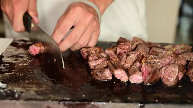 Cutting Seared Beef Strips into Cubes on Wooden Cutting Board for Cooking