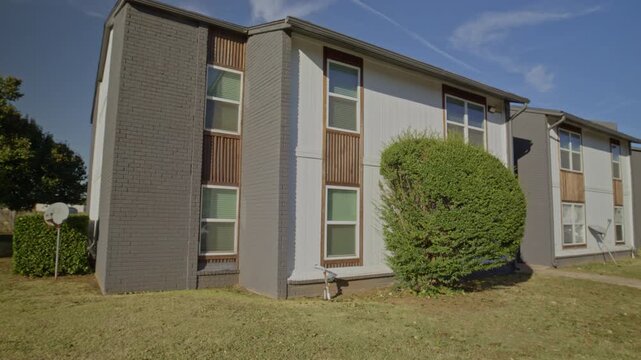 Sunny daytime shot of a two-story corner brick multifamily housing building with lawn and satellite dish.