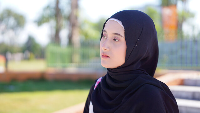 Young Asian Muslim Woman in Black Hijab Sitting on Outdoor Park Stairs Looking Away Thoughtfully in Modest Fashion Attire