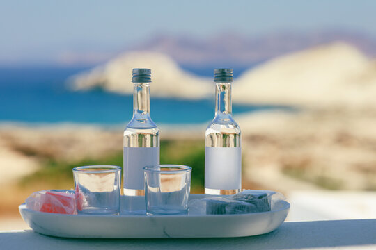 Two bottles of the Greek spirit, Ouzo with glasses on a tray overlooking Mandrakia, Milos, Greece symbolizing hospitality, celebration, and Mediterranean tradition.