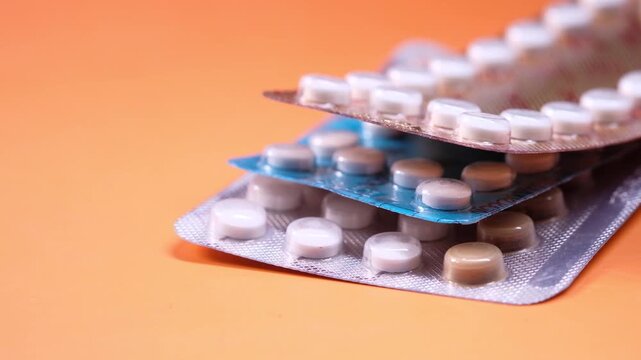 A close-up view of several birth control pill blister packs stacked on a vibrant orange background, highlighting contraceptive methods and family planning