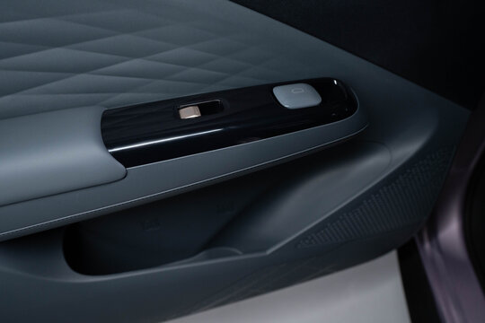  Close‑up of modern car interior door panel featuring quilted upper design, matte armrest, and glossy black trim with integrated lock and power window buttons.