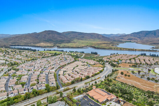 An aerial view of a large housing community near Otay Lakes in Chula Vista featuring dense suburban single-family blocks, winding green parkways, and close proximity to the Lower Otay Lake reservoir