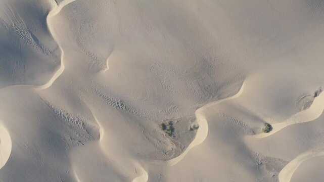 Aerial drone view of the vast, undulating Maspalomas sand dunes on Gran Canaria. The camera booms up, revealing the intricate patterns and textures of the desert landscape.
