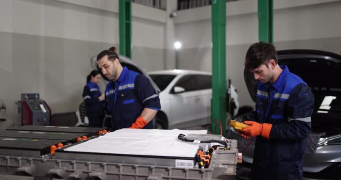 Professional EV technicians performing high-voltage battery diagnostics and electrical testing in a modern electric vehicle service workshop.