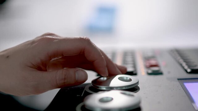 A close-up of a person's hand adjusting a knob or dial on a professional studio mixing console in a broadcast or recording studio.
