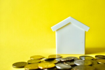 White toy house model with a pile of Malaysian coins in the foreground, isolated on a vibrant yellow background. Concept for home savings, real estate investment, property tax, and mortgage planning. © Akram
