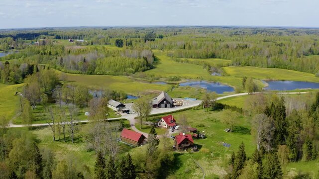 Aerial view of a rustic country farm house and outbuildings surrounded by green forests and lakes. Verdant countryside landscape in Europe.