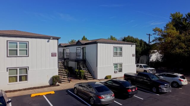 Sunny daytime shot of a two-story multifamily housing building with exterior stairs and adjacent parking lot.