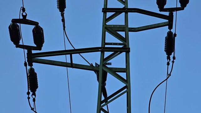 Silhouette of lattice steel power transmission tower beneath clear blue sky, with insulators, cables, and crossbeams creating strong industrial utility scene for energy distribution and engineering