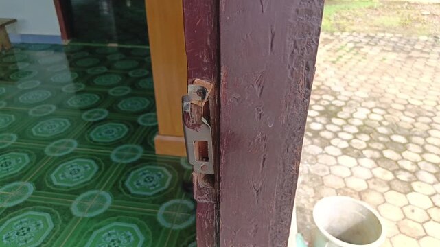 Stock video showing a bent, rusty door latch keeper plate damaged and misaligned on an old painted wooden door jamb.
