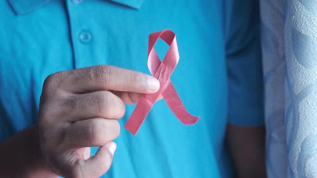 Person holding red awareness ribbon against blue polo shirt representing world aids day support and solidarity