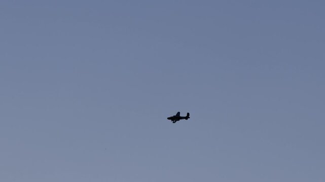 Silhouettes of two propeller planes flying in formation against a blue sky
