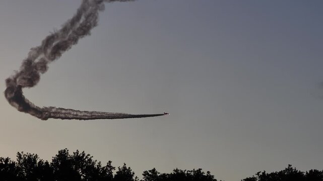 Airplane performing aerobatic maneuvers with smoke trail against sky
