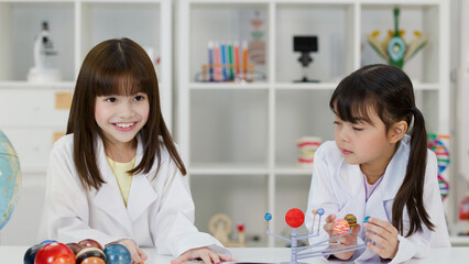 Two Elementary School Girls in Lab Coats Studying Solar System Model © blueringmedia