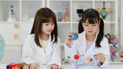 Two Elementary School Girls in Lab Coats Studying Solar System Model © blueringmedia